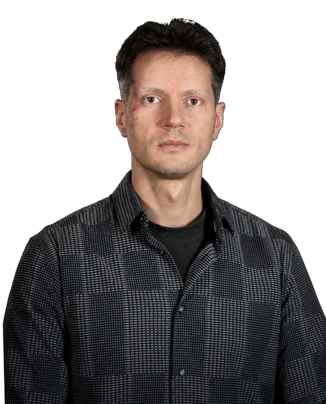 Portrait photograph of David Siewert against a plain white background. He has short dark hair, wears a dark patterned button-up shirt over a black t-shirt, and looks directly into the camera with a calm, neutral expression.